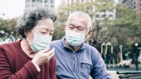 Woman and man sit in park wearing masks